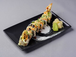 Gourmet sushi roll topped with sauce and garnishes, served with wasabi and pickled ginger on a black plate in elegant Japanese dining style