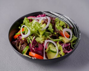 Fresh mixed salad with lettuce, cucumber, tomato, avocado, and onion rings served in a black bowl, representing healthy and balanced eating