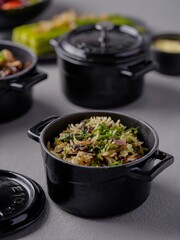Cooked rice with vegetables and herbs served in a small black pot, styled with other side dishes for a rustic gourmet presentation