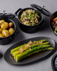 Assorted side dishes including potatoes, asparagus, salad, rice, and vegetables served in black bowls and plates, styled for a gourmet presentation
