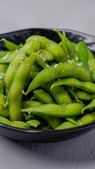 Steamed edamame beans sprinkled with sea salt, served in a black bowl for a healthy and fresh appetizer presentation