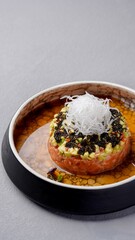 Gourmet tuna tartare topped with avocado, seaweed, and shredded radish, served in a shallow bowl with sauce for an elegant fine dining presentation