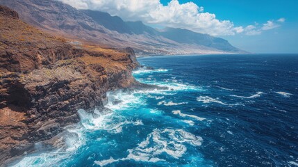 Drone view of Tenerife south coast with Atlantic ocean and strong swell beating against the walls of a rocky cliff, blue rough sea with big waves with foam crashing against the rocks