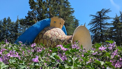 A vibrant, colorful giant snail sculpture is nestled among a variety of blooming flowers in a...
