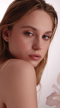 Beautiful woman in white top, blonde hair and neat makeup poses in front of camera with lily flower in hand. Beauty face.