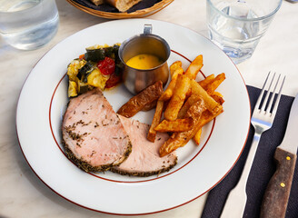 Grilled pork steak sliced on plate with fried potatoes, sauce, and vegetable garnish