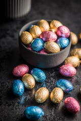 Chocolate easter eggs wrapped in multi colored foil in bowl on black table.