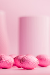 Chocolate easter eggs wrapped in pink colored foil on pink background.