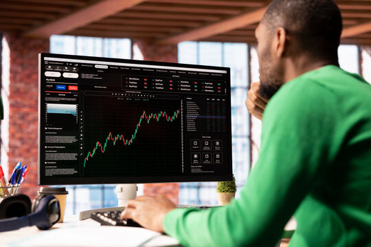 Day trader using computer, purchasing stocks that might perform well and selling ones that might drop in value. Forex trader browsing though stock exchange portfolio pages at PC desk