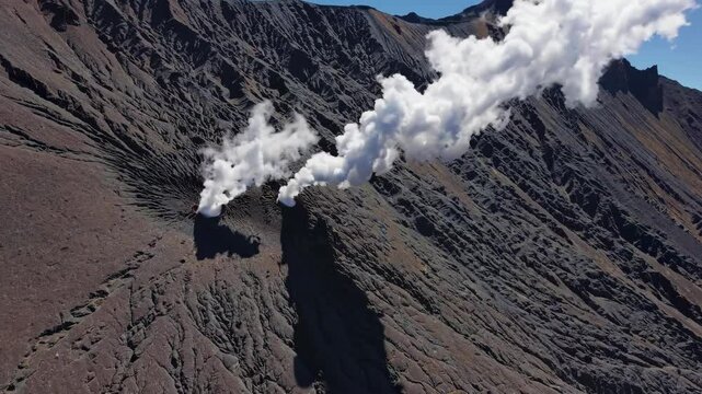 White smoke billowing from Mount Bromo crater, revealing powerful volcanic activity across East Java's dramatic landscape with geothermal emissions rising against rugged terrain