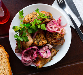 Oriental grilled pork meat shashlik with sliced onion rings on a white ceramic plate
