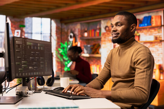 Happy man working in AI tech agency providing custom software development services. Cheerful african american IT expert using machine learning to streamline coding process in startup office - Powered by Adobe