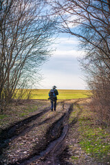 Obraz premium Man walking on dirt road towards green field against blue sunset sky
