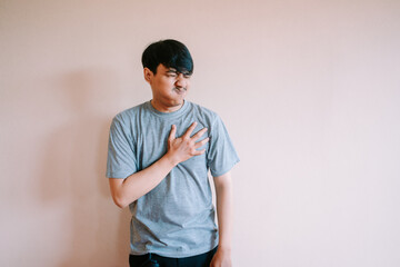 Man experiencing chest discomfort with hand on heart against plain wall