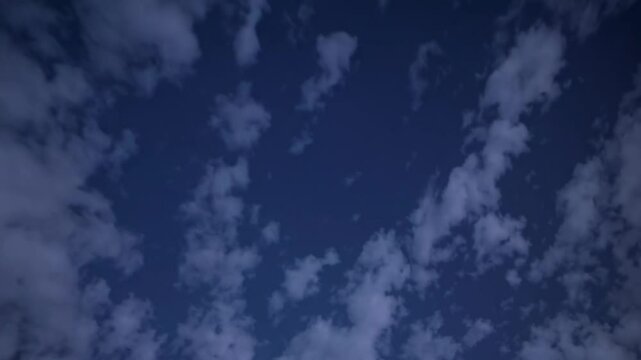 Soft white clouds drifting languidly across deep blue twilight sky, creating mesmerizing atmospheric cloudscape with serene evening light
