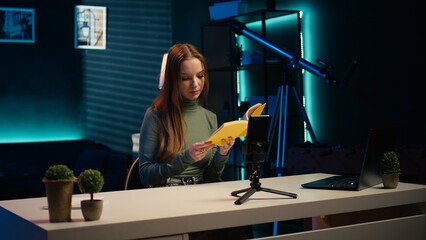 Young influencer filming review of light bulb able to change into different colors. Content creator showcasing smart home automation technology in apartment studio, camera B
