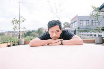 Thoughtful man rests on table, gazing intently at the camera outdoors
