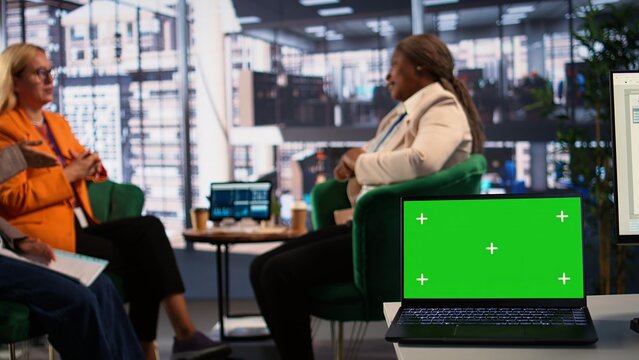 Diverse goals oriented businesswomen look at isolated mockup during a meeting, solving tasks for the monthly revenue balance. Group of experts planning a new strategy. Camera B.