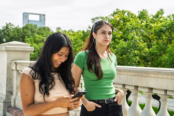 Naklejka premium Two young women using smartphone outdoors in urban park