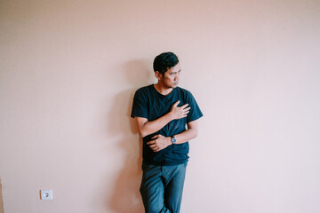 Contemplative asian man leaning against the wall with hand on chest