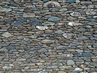 A wall made of stone with a greyish color. The wall is made of small stones and has a rough texture