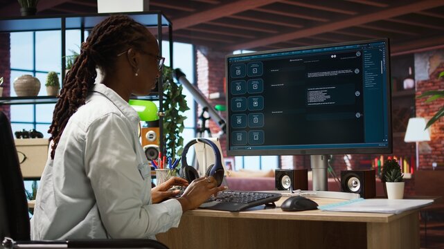 Woman seated at desk using AI LLM chatbot software in modern urban home office. Person requesting help from large language model program on computer in bright apartment workspace, camera A