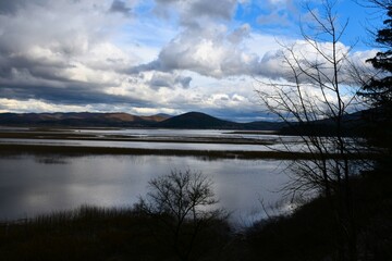 Obraz premium View of Cerknica lake with hill behind and clouds in the sky in Notranjska, Slovenia