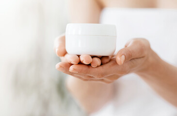 Unrecognizable lady wrapped in towel after shower with cream jar, body care concept, free space