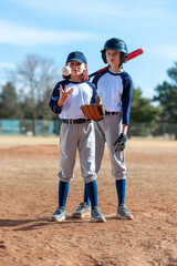 Obraz premium Two young girls in little league baseball uniforms with bat, ball, glove and helmet at home plate