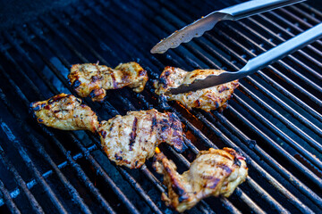 Grilling Juicy Chicken Pieces on Outdoor Barbecue with Tongs