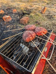 Juicy burgers are sizzling enticingly on a portable grill set up at a scenic and beautiful outdoor location