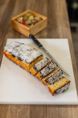 Freshly sliced coconut and chocolate cake on a white cutting board with a knife beside it. Soft texture, golden crust, wooden table, raspberries in the background, blurred focus, warm lighting.