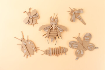 Cardboard insects for kids’ crafts, dragonfly, caterpillar, butterfly, and ladybug made from cut paper, cardboard box activities, creative happy playtime, brown paper texture on peach surface