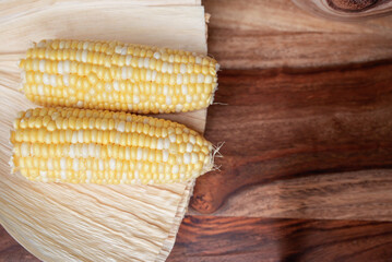 Two Fresh Corn on the Cob Placed on Husk with a Rustic Wooden Background
