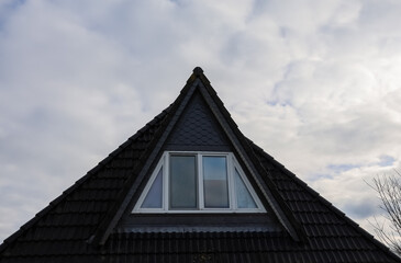 Triangular dormer window with black roof tiles under cloudy sky