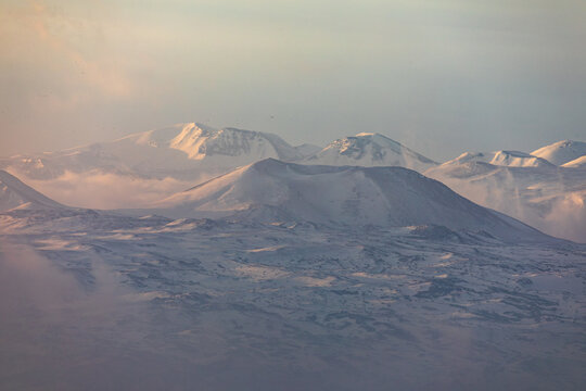 Snow-covered peaks of the Geghama mountain range, including Mount Azhdahak, rise above Lake Sevan in Armenia. A breathtaking winter sunrise landscape with mist and soft sunlight