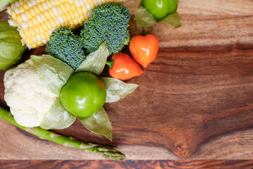 Fresh Assorted Vegetables Including Tomatillo, Broccoli, Corn, and Peppers on a Wooden Cutting Board