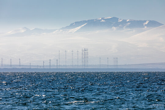 Snow-covered peaks of the Geghama mountain range, including Mount Spitakasar, rise above Lake Sevan in Armenia. A breathtaking winter morning landscape with mist and soft sunlight