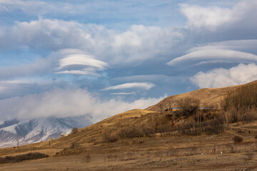 Lenticular clouds weather phenomenon over the landscapes of Syunik (Zangezur), Armenia. These unique cloud formations create a dramatic and atmospheric scene over rolling hills and open skies.