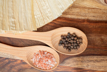 Himalayan Salt and Black Peppercorns in Wooden Spoons on a Rustic Background