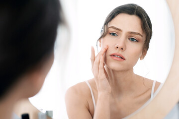 Acne prone skin concept. Upset young woman looking at mirror at home, checking her face skin