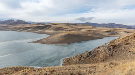 The eroded shoreline of Tolors Reservoir in Syunik (Zangezur), Armenia, features layered sediment formations shaped by natural erosion, hydrology, and geological processes
