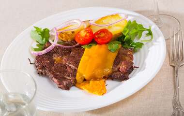 Well-cooked beef steak with cheese and baked potatoes served at plate with tomatoes