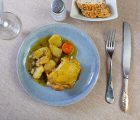 Delicious baked chicken thigh and drumstick served on plate with side dish of stewed potatoes. Hearty homemade dinner