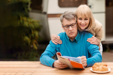 Mature woman helping her husband solve crossword puzzle near trailer outside