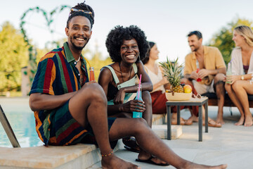 Young couple enjoying drinks by the pool during a summer party with friends
