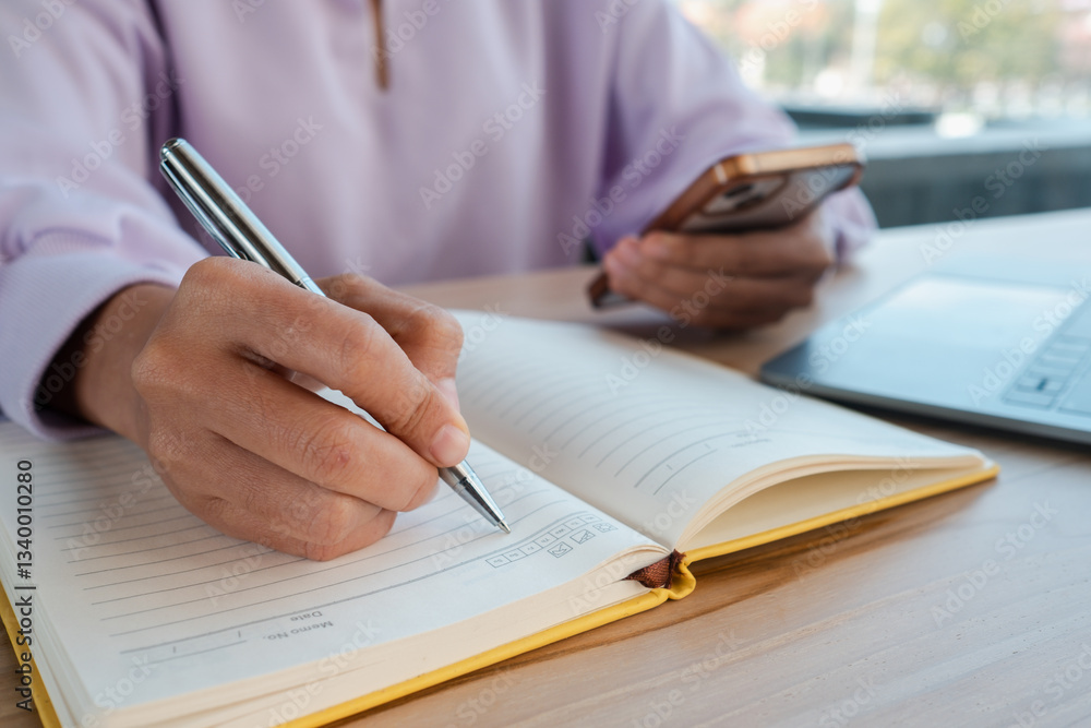 Poster close-up of a person writing in a notebook while holding a smartphone, showcasing multitasking in a 