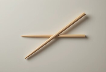 A pair of wooden chopstick rests diagonally on a smooth, neutral surface. Soft lighting highlights its texture and clean edges, creating a minimalist, balanced composition.
