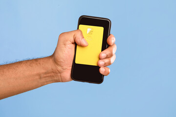 A young African American man isolates himself in a bright setting while holding a smartphone with a yellow card. The simplicity of the moment highlights modern lifestyle choices.