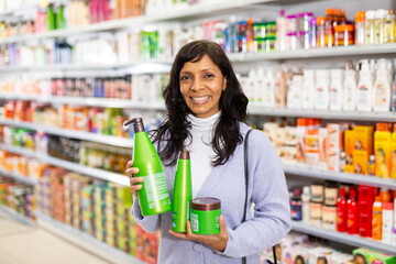 Portrait of smiling hispanic woman shopping in cosmetics store, choosing hair care treatments..